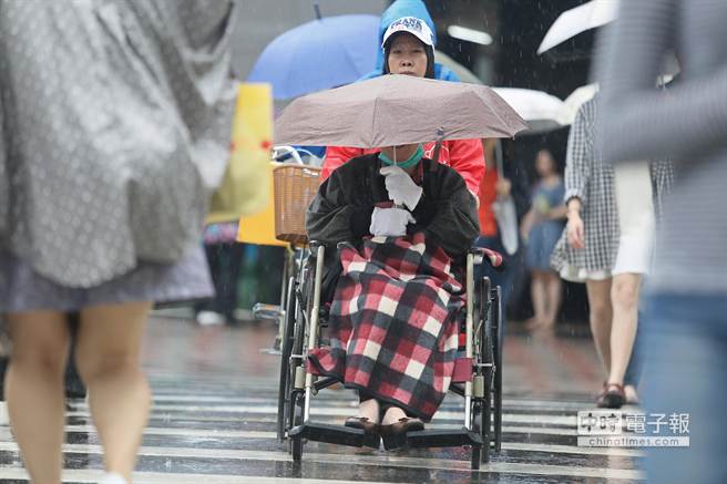 臺灣中部以北從中午開始雨勢增大，連坐輪椅外出的民眾都撐起傘具避雨。(中時電子報圖張鎧乙攝)