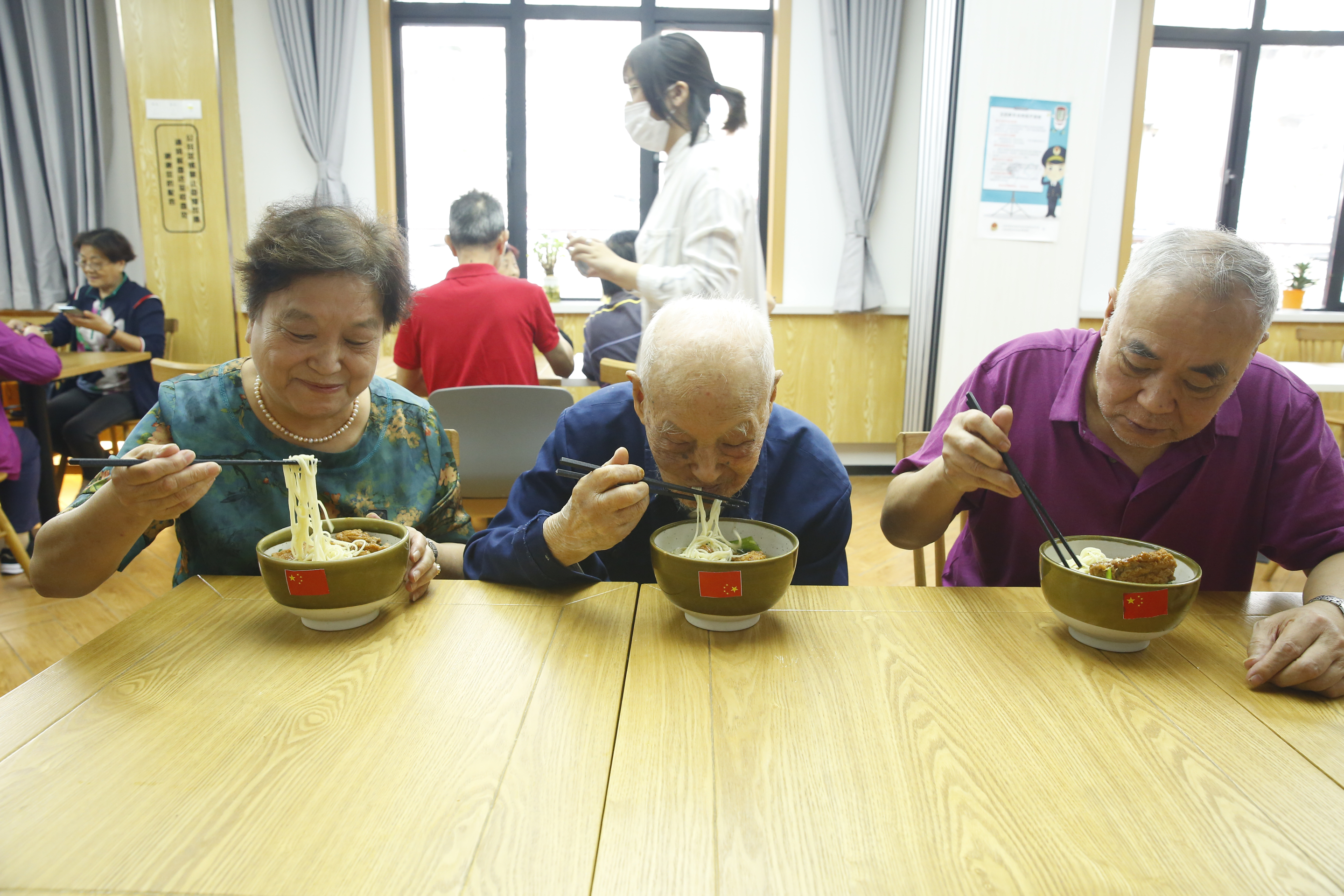 來自普陀區(qū)石泉路街道鎮(zhèn)坪居民區(qū)106歲的李佩印老人（前排右二）正在和居民朋友一起吃國慶面。石泉路街道 供圖